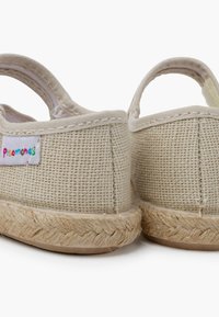Beige kanvas espadrillos med en vævet tekstur, elastiske remme og en flettet jute-sål. Indeholder en farverig etiket på siden.