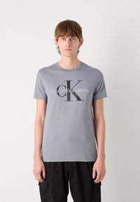 Gray cotton t-shirt featuring a prominent black logo reading "Calvin Klein Jeans" with a round neck and short sleeves.
