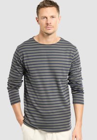 Maglietta a maniche lunghe di colore verde oliva con righe orizzontali blu navy, dotata di scollo rotondo e vestibilità rilassata. Tessuto morbido con spacchi laterali.