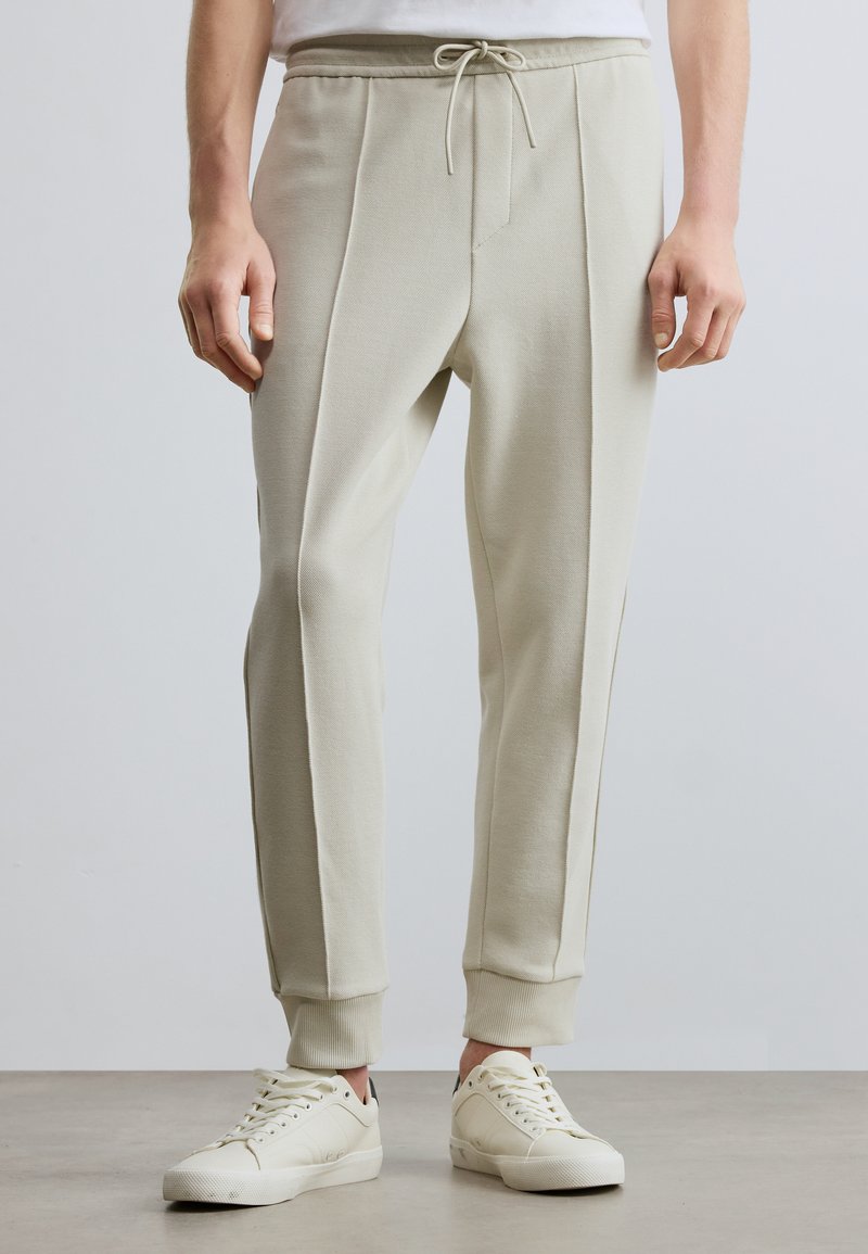 Vaaleanbeiget joggers-housut, jotka on valmistettu pehmeästä kankaasta, ja joissa on kiristysnauhavyötärö, sivutaskut sekä kapenevat nilkkapitolaiset.