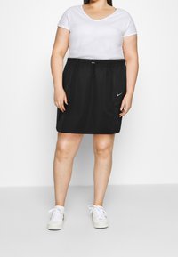 Černá sportovní sukně Nike s elastickým pasem a šňůrkou, se bočními kapsami. Spárována s bílým tričkem s výstřihem do V a bílými teniskami.