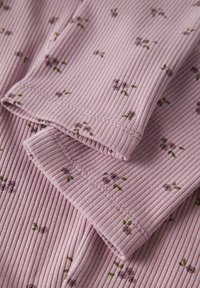 Różowa prążkowana tkanina z małymi fioletowymi wzorami kwiatowymi i zielonymi liśćmi, prezentująca złożone krawędzie i widoczne szczegóły szycia.