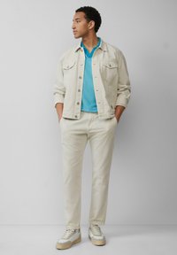 Veste en jean de couleur claire sur une chemise polo turquoise, associée à un pantalon de couleur crème et des baskets beiges avec des accents blancs.