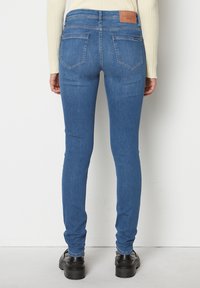 Blugi skinny de culoare albastru mediu din denim, cu talie medie, două buzunare la spate și un eticheta de piele maro pe talie.