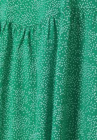Tessuto verde con piccoli pois bianchi e una lavorazione arricciata, che mette in risalto una consistenza liscia e un aspetto fluido.