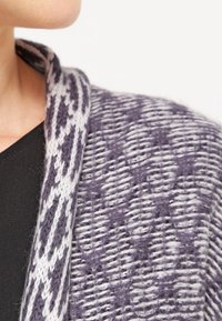 Fialový a šedý pletený cardigan s texturovaným vzorem, který má široký límec a měkkou, huňatou látku. Detailní pohled z ramene.