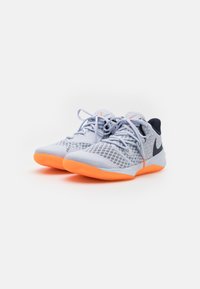 Scarpe sportive grigio chiaro con tomaia in rete traspirante, suole arancioni e dettagli neri. Presentano lacci e un design testurizzato.