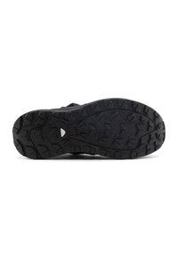 Suela de zapato deportivo negro con surcos profundos y multidireccionales y bordes curvados, que presenta una superficie texturizada y un área de puntera reforzada.