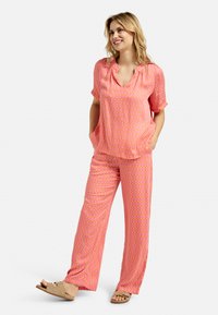 Rosa gemustertes Schlafanzugset mit kurzen Ärmeln, einem V-Ausschnitt-Top mit Seitentaschen und weit geschnittenen Hosen aus einem glatten, leichten Stoff.