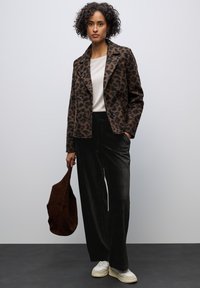 Kabát s leopardím vzorem v hnědé a černé látce, bílý top, tmavé sametové kalhoty, hnědá taška a bílé tenisky.