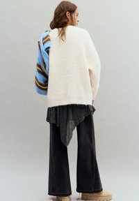 Túlméretezett krémszínű kötött pulóver világoskék és barna csíkos díszítéssel; fekete aszimmetrikus ing és sötét, bőszárú farmer nadrág fölött viselve.