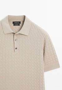 Beige katoenen poloshirt met kabelgebreide textuur, twee knopen aan de sluiting en een geribde kraag en mouwen. Merklabel zichtbaar bij de halslijn.