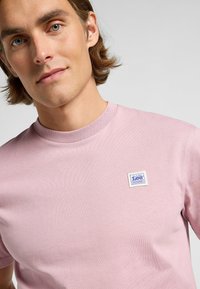 Lyserød bomulds t-shirt med rund halsudskæring og et lille blåt og hvidt label på brystet. Glat tekstur med normal pasform.