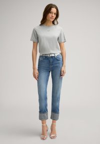 Grijze katoenen t-shirt met korte mouwen, gecombineerd met lichtblauwe spijkerbroek met een gemusterde omslag en een metallic riem. Zilveren hakken maken de look compleet.