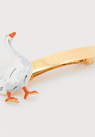 Κλιπ μαλλιών σε χρυσό τόνο με σχέδιο λευκής και γκρι χήνας με πορτοκαλί πόδια και ράμφος. Περιλαμβάνει χαραγμένο λογότυπο "Moschino".