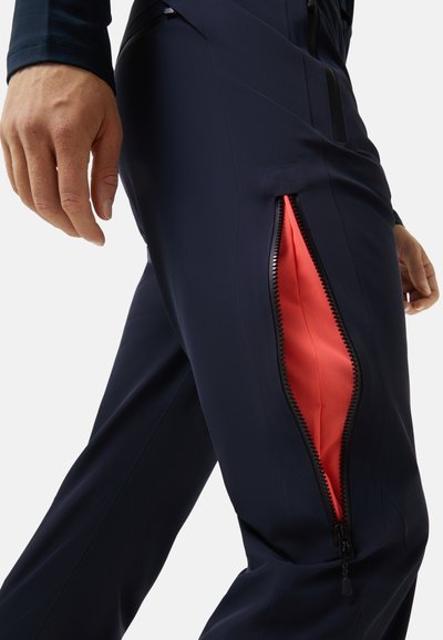 Pantalons bleu marine avec une finition texturée dotés d'une fermeture éclair sur le côté révélant un intérieur corail vif. Conçus pour la fonction et le mouvement.
