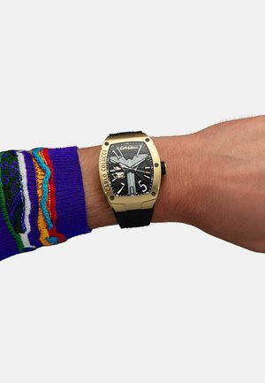 Black dial watch with gold case, rectangular shape, rubber strap, bold hour markers, and visible movement details on the dial.