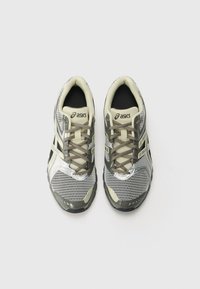Chaussures de sport grises et noires avec des panneaux en maille, bout rond, lacets contrastants et logo sur la languette. Design léger pour le confort.