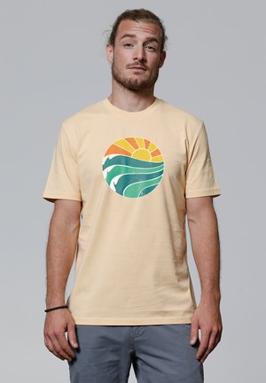 Lichtgele katoenen T-shirt met een rond grafisch ontwerp van golven en een zon in oranje en groene tinten. Korte mouwen, ronde hals.
