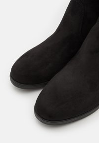 Svarta mockaankelstövlar med en slät yta, rundad tå och subtila sömdetaljer, mot en vit bakgrund.