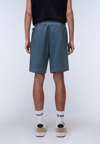 Blue cotton shorts with an elastic waistband, side pockets, and a relaxed fit, paired with beige sneakers and white patterned socks.