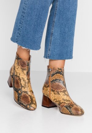 Ankelhøje støvler i brun og beige slangeskindsmønster med træblokhæle, båret sammen med cropped blå jeans.