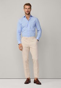 Lichtblauwe overhemdd met lange mouwen, gecombineerd met beige slim-fit broek en bruine loafers. Gladde stof, slim fit en subtiele details op het overhemd.