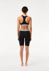 Completo sportivo nero composto da reggiseno e pantaloni corti, con un design a schiena scoperta e una fascia a righe in vita. Il tessuto è liscio e aderente, ideale per l'abbigliamento sportivo.