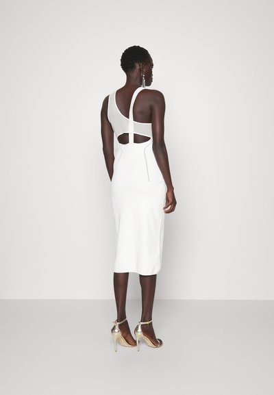 Vestito bianco aderente con una spalla e un dettaglio cut-out sul retro. Tessuto liscio di lunghezza media fino al polpaccio, abbinato a tacchi dorati.