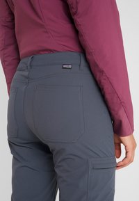 Grå, stretchiga byxor med sid- och bakfickor, med en medelhög midja. Accentuerade med kontrasterande sömmar och en logotyp.