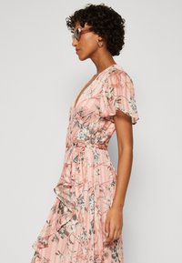 Pink floral wrap dress featuring a deep V-neck, short flutter sleeves, cinched waist, and layered ruffled hem. Smooth, textured fabric.