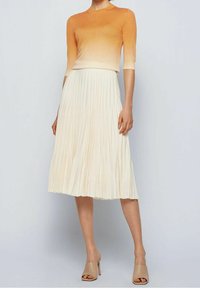 Grönsaksfärgad till krämfärgad gradient stickad topp med korta ärmar, matchad med en veckad elfenbensfärgad midi kjol. Outfiten har en jämn textur och flöde.