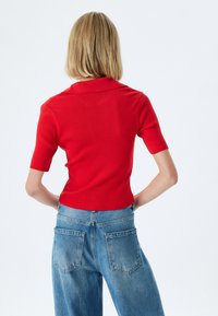 Polo shirt rouge à rayures avec des manches courtes et un col, associé à un jean en denim bleu clair taille haute avec des poches arrière.