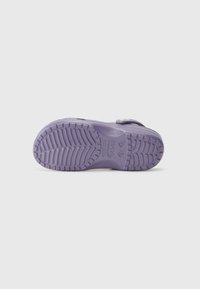 Purple rubber shoe sole with textured grip pattern and heel support. Features a circular strap adjustment on one side. Flat and lightweight design.