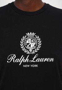 Camiseta de algodón negra con un logotipo blanco que presenta un diseño de corona y laurel, y el texto "Ralph Lauren NEW YORK" en la parte inferior.