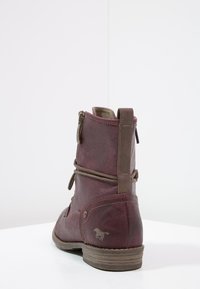 Botín de tobillo burdeos con acabado texturizado, cremallera lateral, cordones decorativos y un pequeño logotipo de caballo en el talón. Suela marrón resistente.