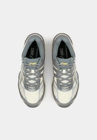 Athletic shoes in gray and cream, featuring mesh fabric, textured panels, lace-up closures, and a patterned sole. Brand logo visible on top.