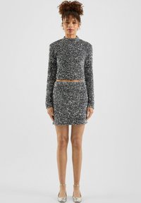 Srebrny crop top z cekinami i dopasowana mini spódniczka; dopasowany krój; długie rękawy; wysoki dekolt; gładka tekstura; metaliczne akcenty na butach.