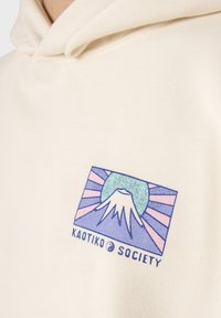 Felpa color crema con cappuccio che presenta un design grafico di una montagna con un motivo a raggi di sole in colori pastello. Include il testo del logo sotto il design.