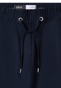 Granatowe spodnie z troczkiem w talii, z metalowymi oczkami, gładką fakturą oraz metką z napisem "CECIL PANTS".