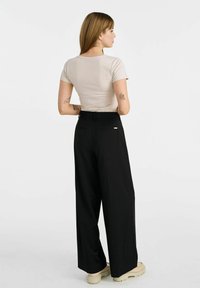 Jasno beżowa dopasowana koszulka z krótkimi rękawami, zestawiona z czarnymi spodniami o szerokiej nogawce z wysokim stanem oraz masywnymi butami w kolorze kremowym.