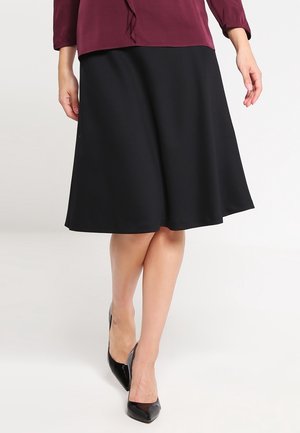 Jupe évasée noire en tissu lisse, atteignant le mollet. Associée à des talons noirs brillants et un haut bordeaux avec un détail volants.