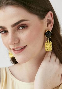 Les boucles d'oreilles en or présentent une pierre précieuse noire en haut, un motif en filigrane doré complexe en dessous, et une finition texturée.