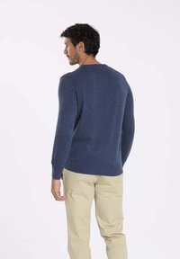 Pull en tricot bleu marine à manches longues, col rond et texture subtile ; associé à un pantalon beige, vu de dos.
