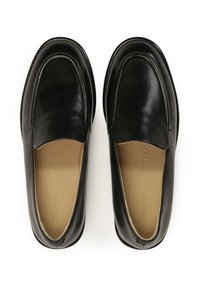 Mocassins en cuir noir avec une surface lisse, bout arrondi et design à enfiler. L'intérieur présente une semelle beige. Accents de couture discrets.