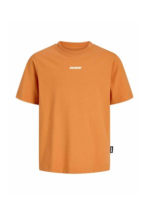 Teenager iført en orange T-shirt, lysegrå jeans, beige sko og en mørkegrøn kasket, stående mod en ensfarvet hvid baggrund.