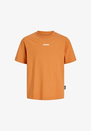 Teenager iført en orange T-shirt, lysegrå jeans, beige sko og en mørkegrøn kasket, stående mod en ensfarvet hvid baggrund.