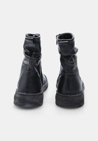 Bottines en cuir noir avec un design flasque, fermeture éclair et semelles en caoutchouc texturé. Détails de couture le long des coutures.