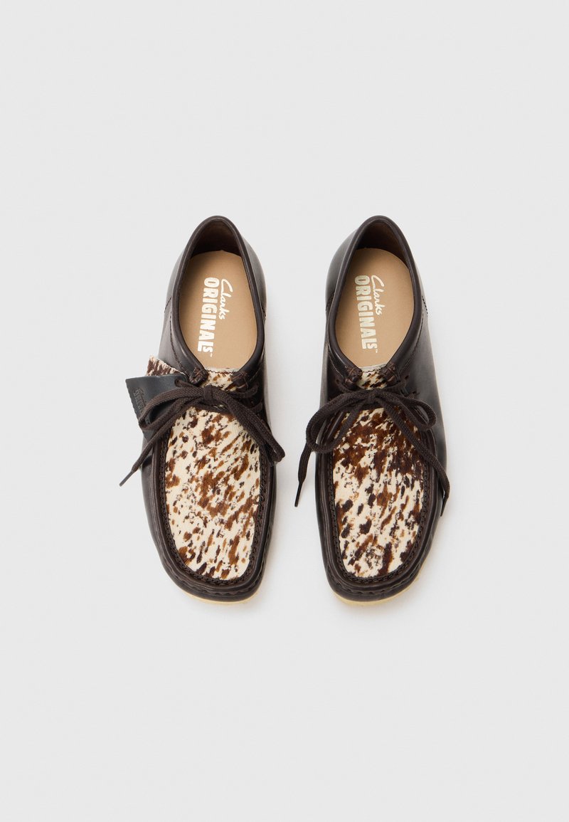 Chaussures en cuir noir avec un dessus texturé crème et marron à motifs, dotées de lacets ronds et d'une semelle intérieure rembourrée. Logo de la marque à l'intérieur.
