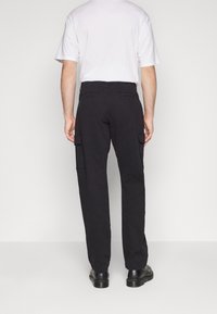 Svarta cargo-byxor med rak bendesign, som har sidofickor och bakfickor. Tillverkade av ett slitstarkt tyg, bärs med en vit skjorta.